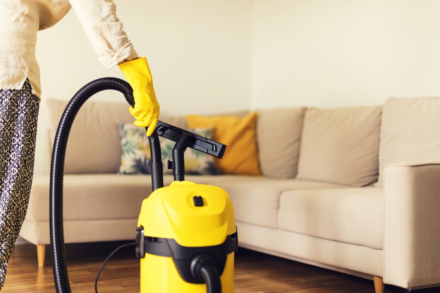 Woman Cleaning Sofa with Yellow Vacuum Cleaner. Copy Space. Cleaning Service Concept